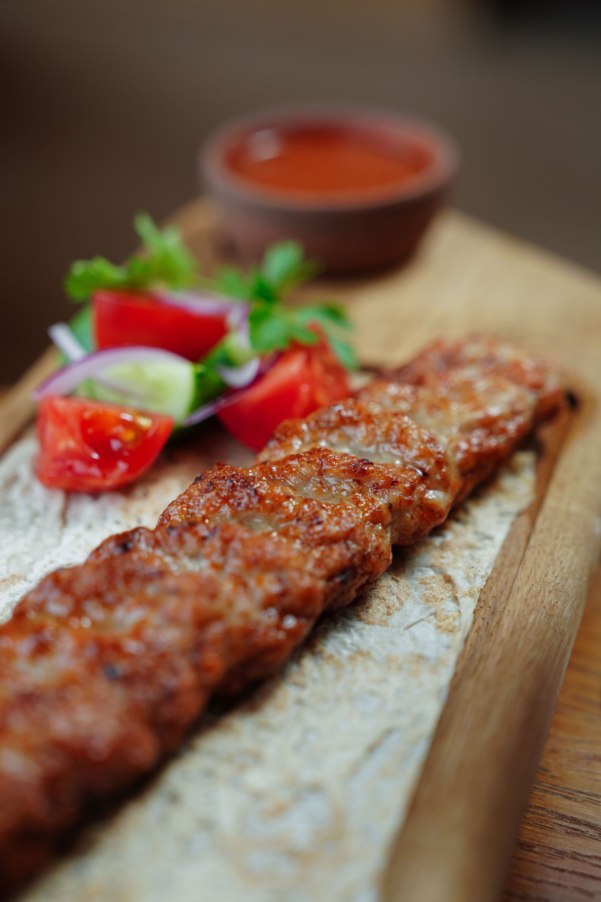 A savory plate of grilled sausages with colorful vegetables and dipping sauce on a wooden tray.